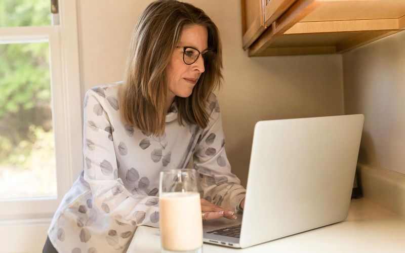 Woman using her computer in the kitchen counter drinking a glass of milk